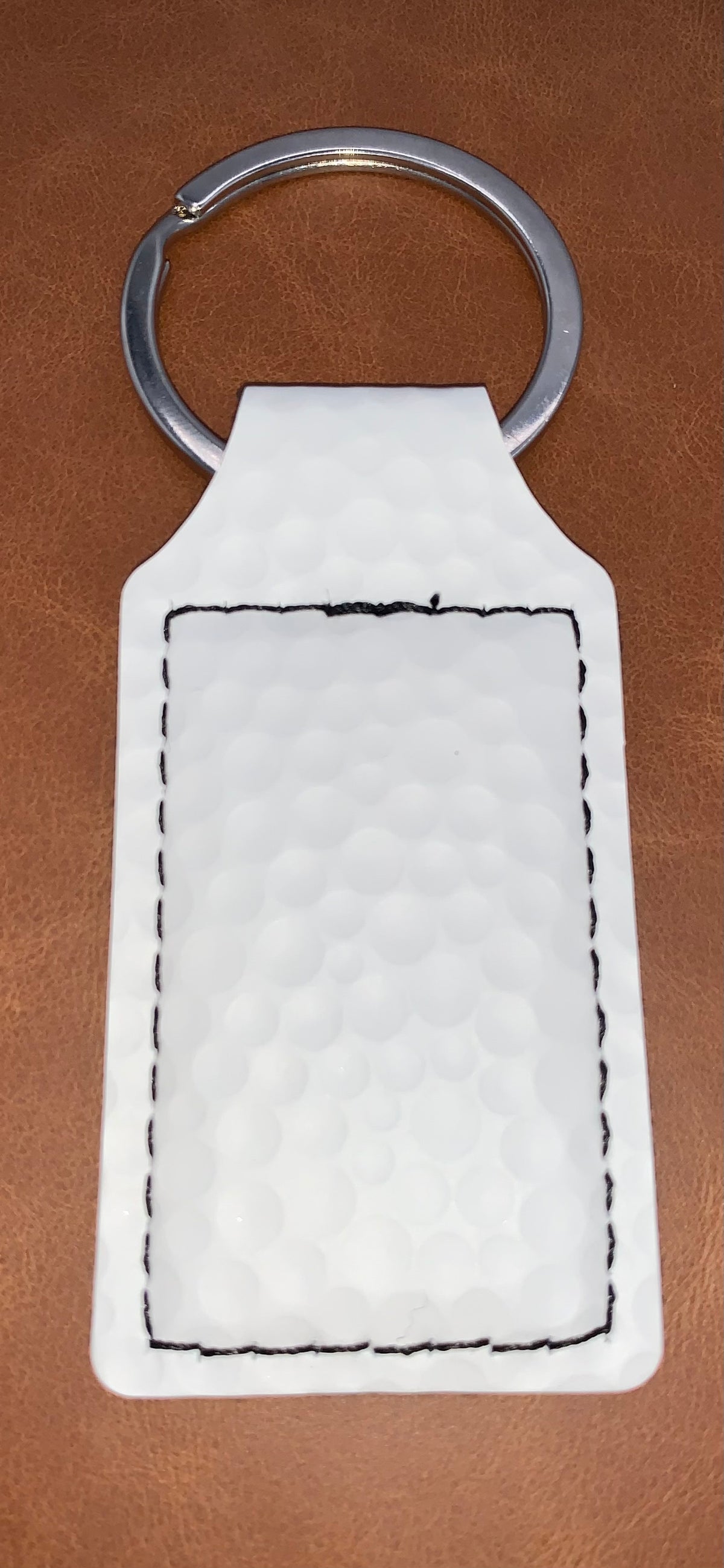 Close-up of the White Golf Texture leatherette keychain showing its raised golf-inspired surface and stitched border.