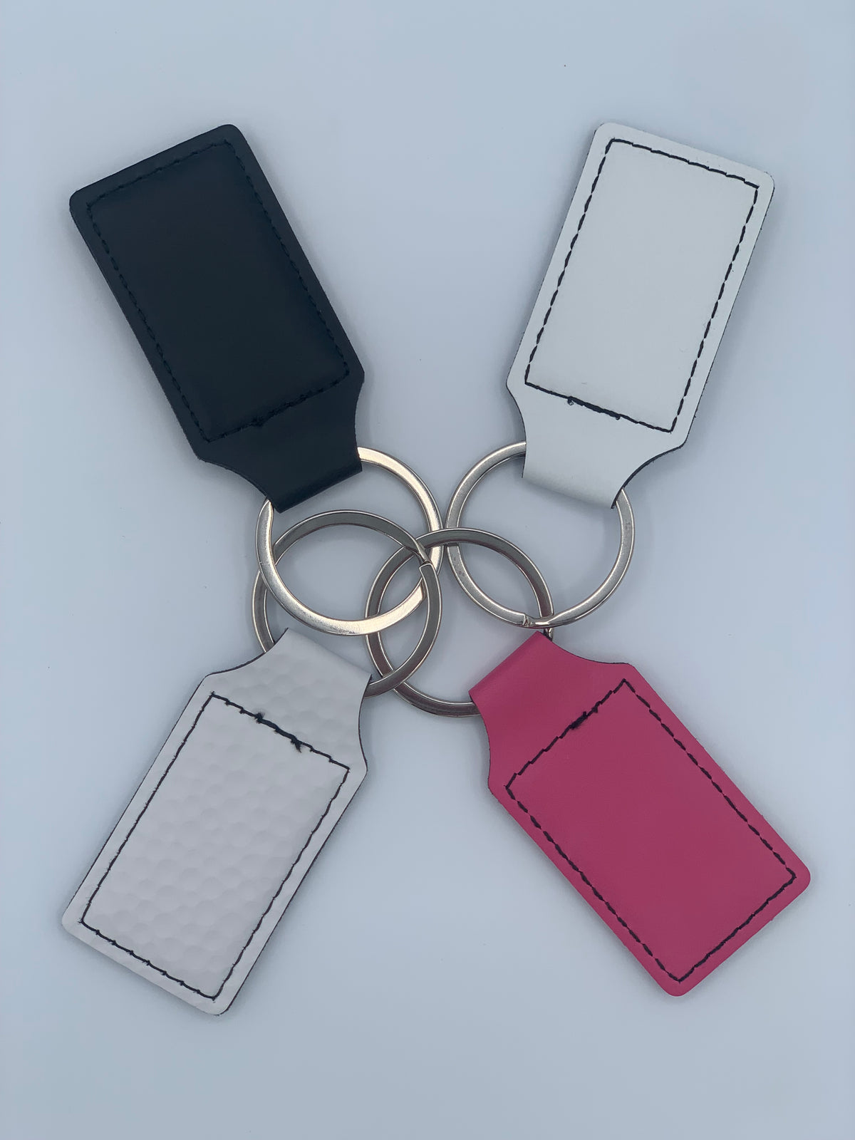 Assorted leatherette keychains shown in Black, White, Primrose Pink, and White Golf Texture finishes.