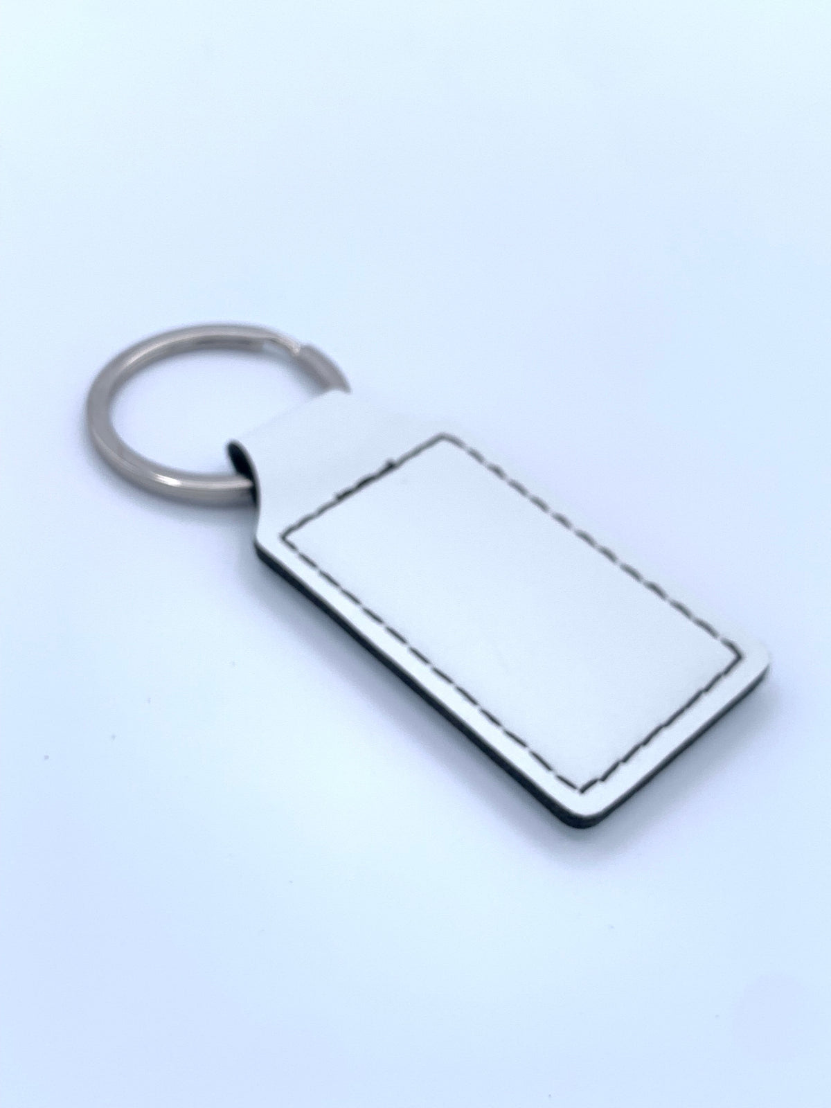 White leatherette keychain shown with attached metal key ring and stitched personalization area.