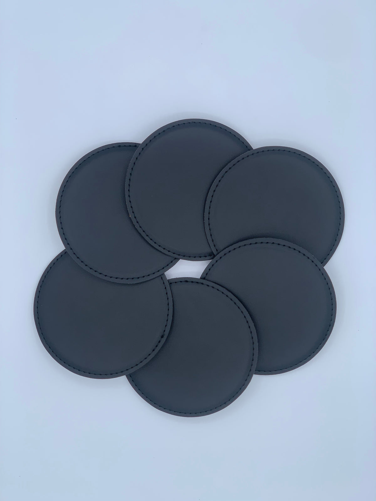 Set of six round black leatherette coasters shown laid out