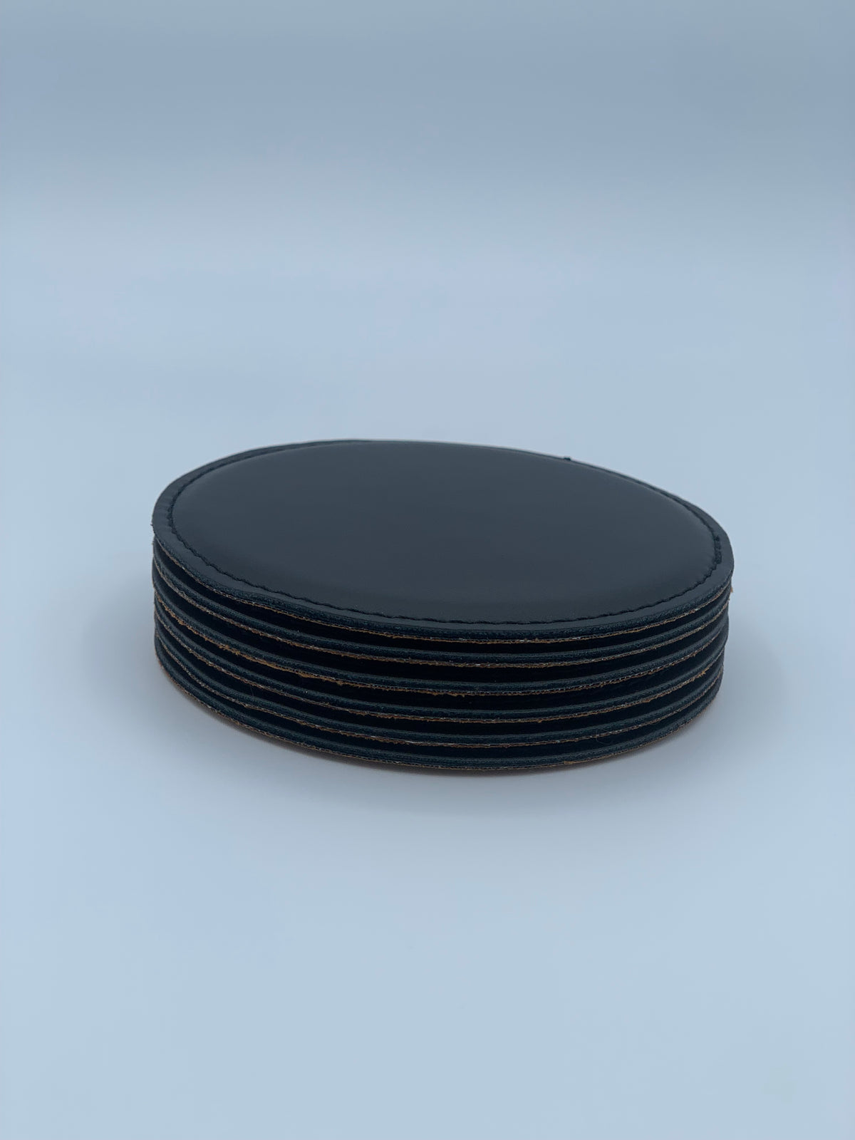 Six round black leatherette coasters stacked together
