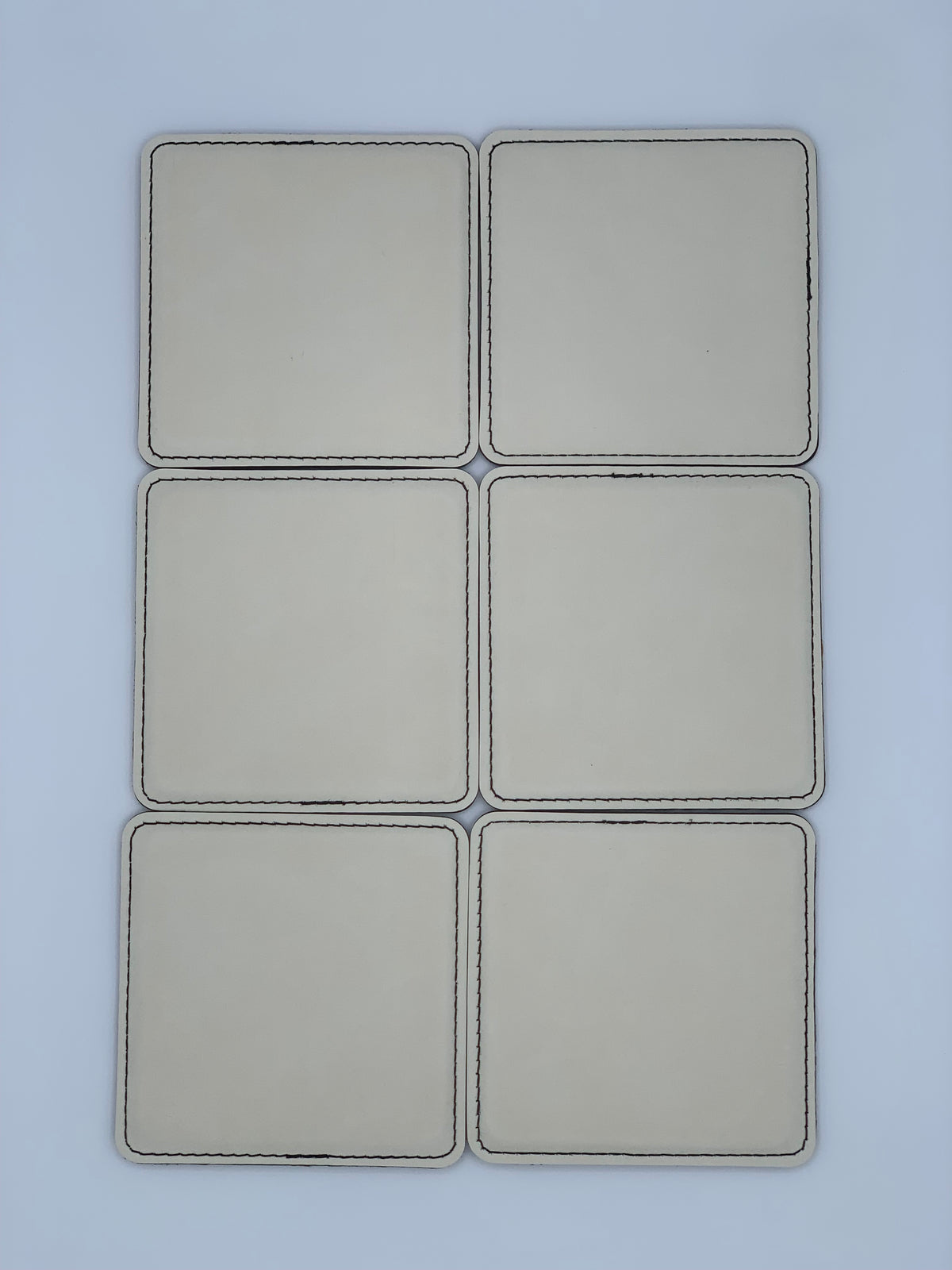 Set of six square light-colored leatherette coasters shown laid out