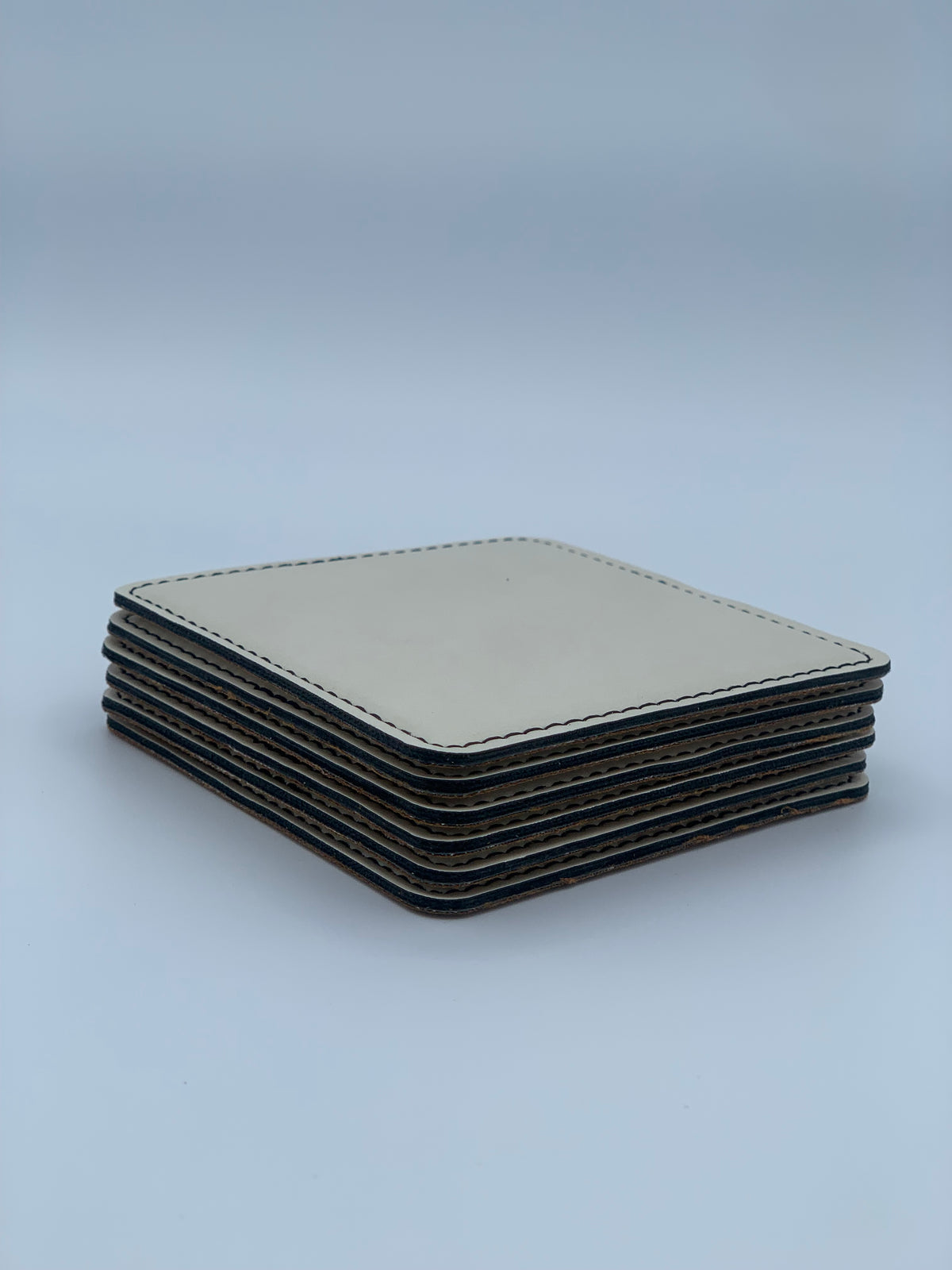 Six square light-colored leatherette coasters stacked together